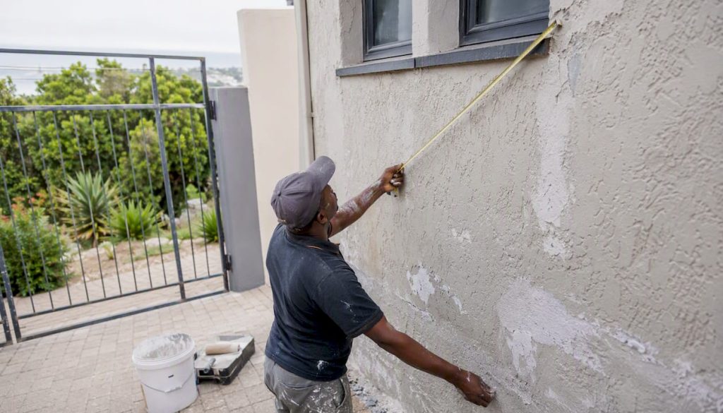 Painter measuring wall area outside home