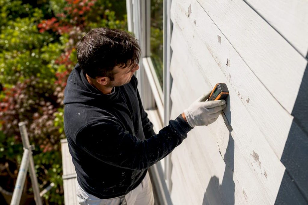 Professional inspecting painted exterior wall closely