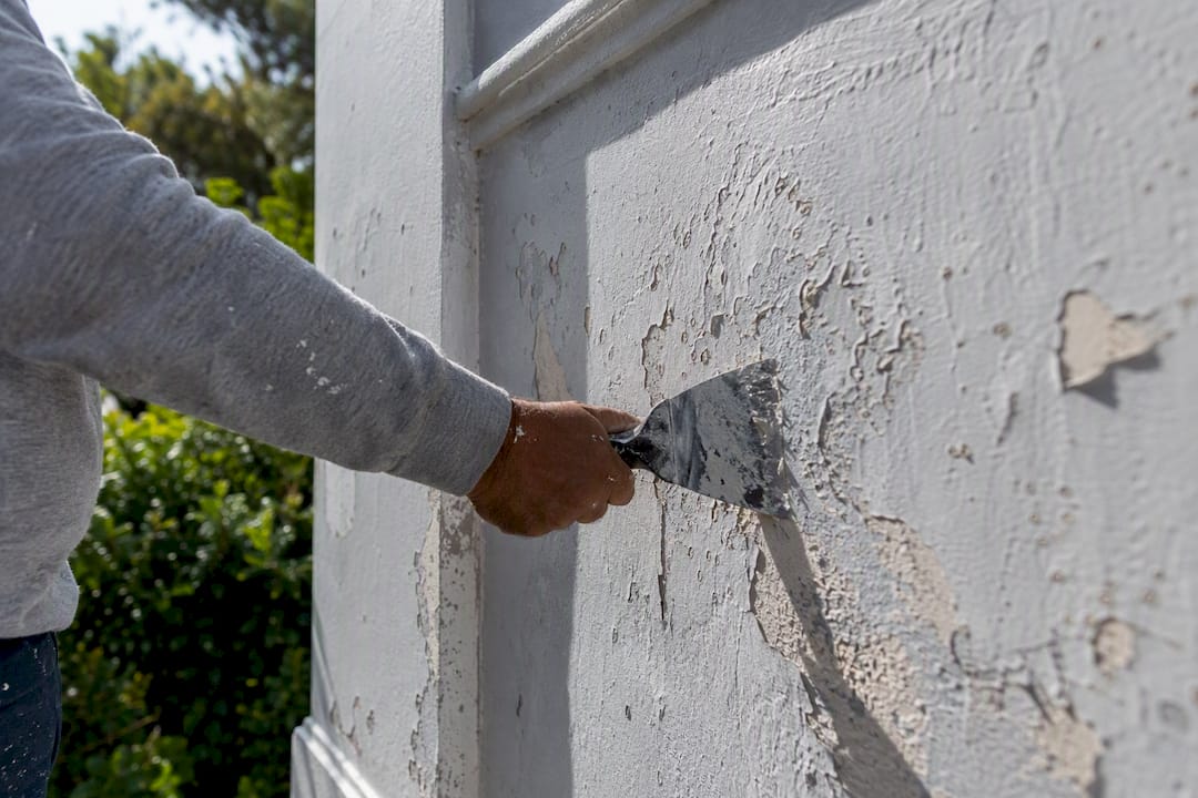Hands scraping old paint on estate wall