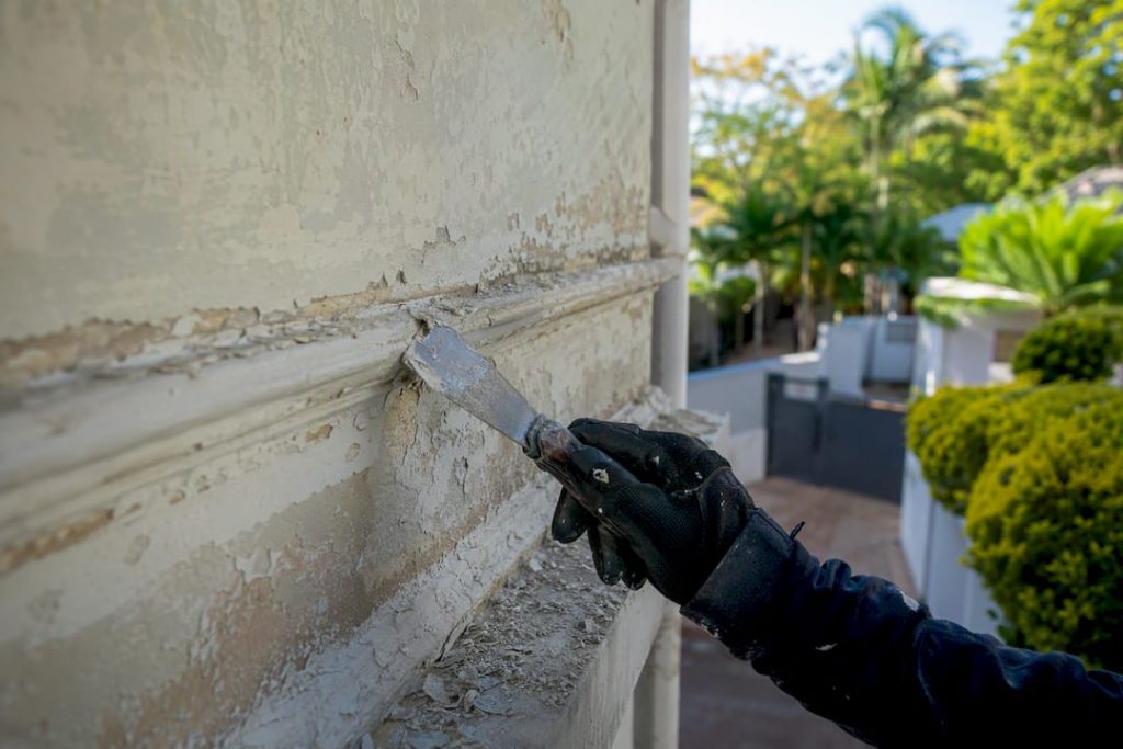 Painter scraping peeling paint on exterior wall